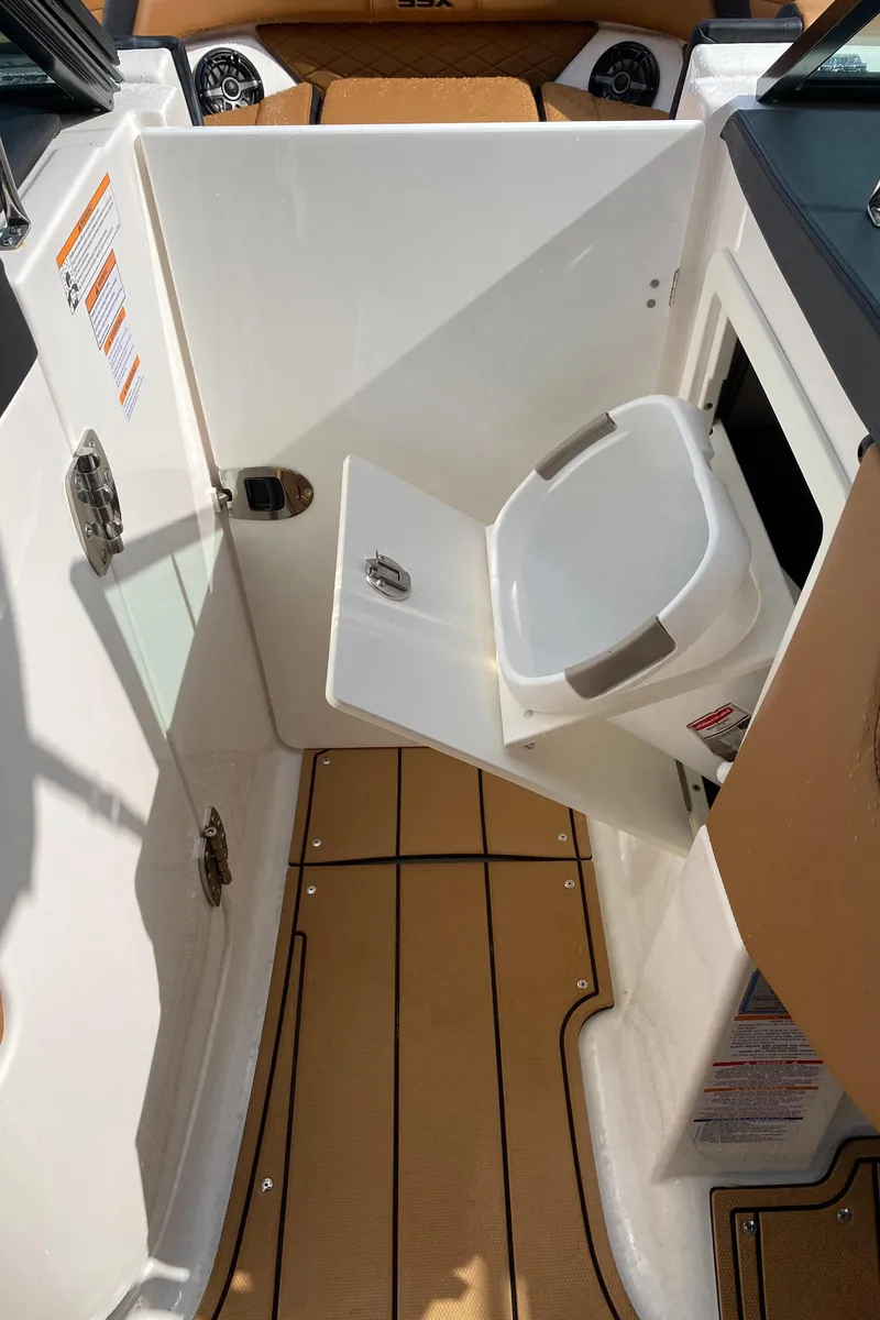 Slide: The Image of 2024 Chaparral 267 SSX boat interior with compact toilet and wooden flooring. - 12