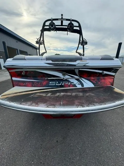 Slide: The Image of 2011 Supra 22v boat rear view with wakeboard tower, parked on pavement. - 3
