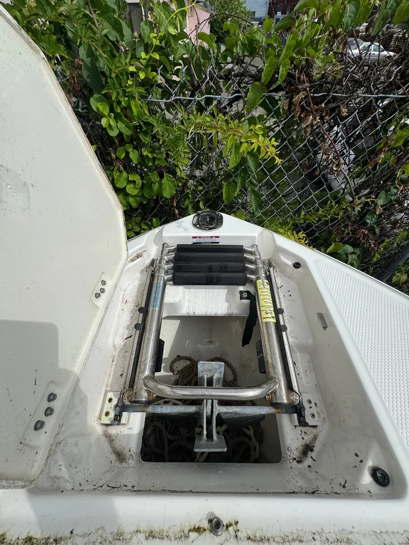 Slide: The Image of 2022 Chaparral 267 SSX OB boat anchor compartment with ladder, surrounded by greenery. - 24