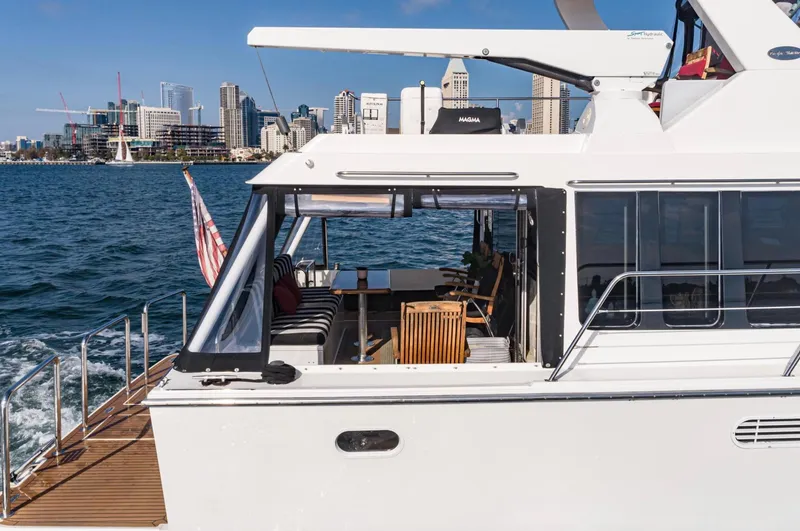 Slide: The Image of 1998 Pacific Mariner 65 Motoryacht cruising near city skyline, featuring spacious deck and seating area. - 21