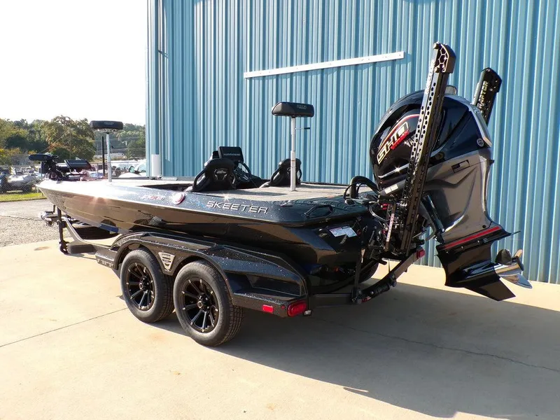 Slide: The Image of 2025 Skeeter FXR20L boat with trailer, parked outdoors near a blue building. - 4