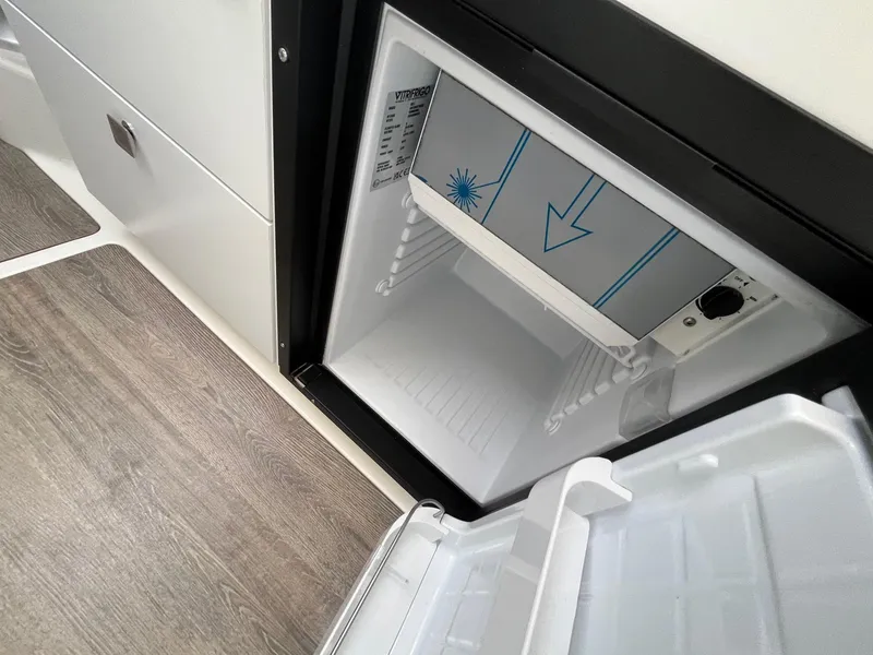 Slide: The Image of 2025 Bayliner Trophy T25 Explorer boat interior fridge, open with visible shelving. - 28