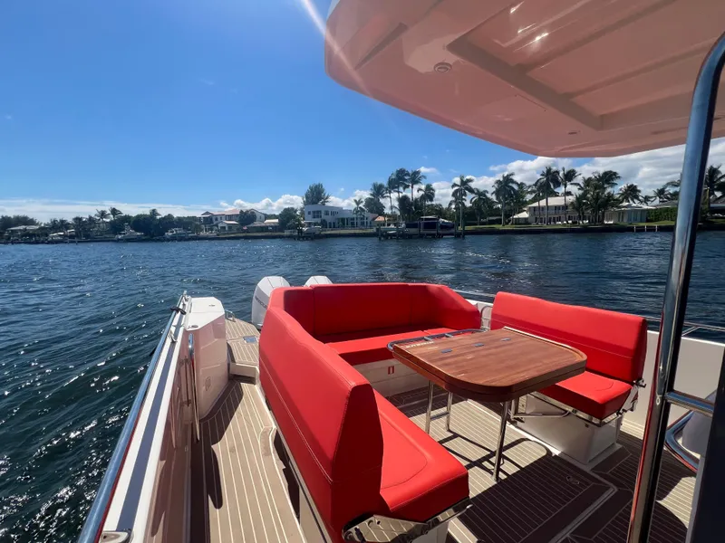 Slide: The Image of Nimbus T11 #98 TRADE! 2022 boat with red seating, wooden table, and scenic waterfront view. - 21