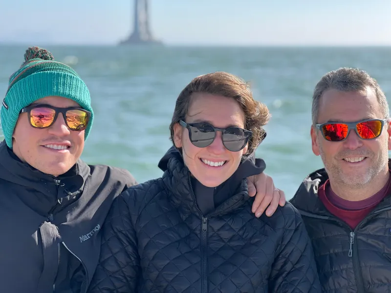Slide: The Image of Three people smiling on a Beneteau 37 sailboat, wearing sunglasses and jackets. - 18