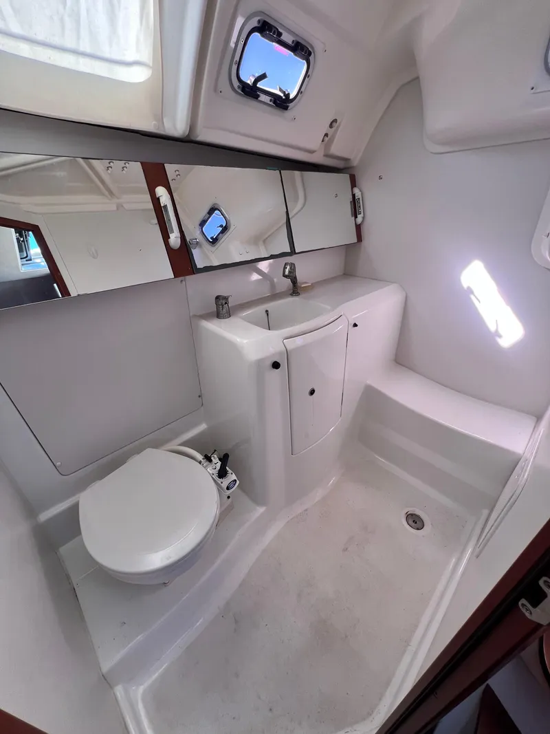 Slide: The Image of 2013 Beneteau 37 yacht bathroom with white fixtures and porthole windows. - 23