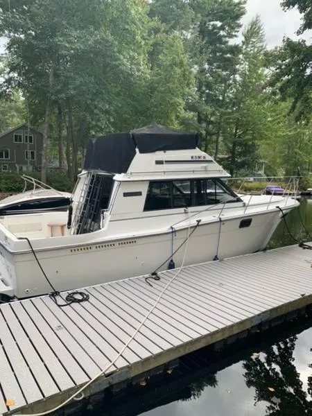The Image of 1985 Carver 3227 Convertible boat docked by a wooded lakeside. - 1