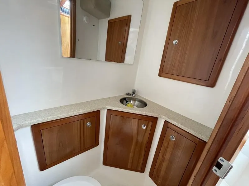Slide: The Image of 2016 Jarrett Bay 32 Walk Around boat bathroom with wooden cabinets and sink. - 48