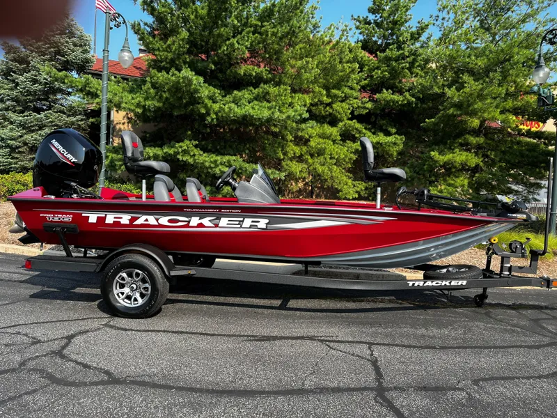 The Image of 2025 Tracker Pro Team 190 boat, red, parked on a trailer, surrounded by trees. - 0