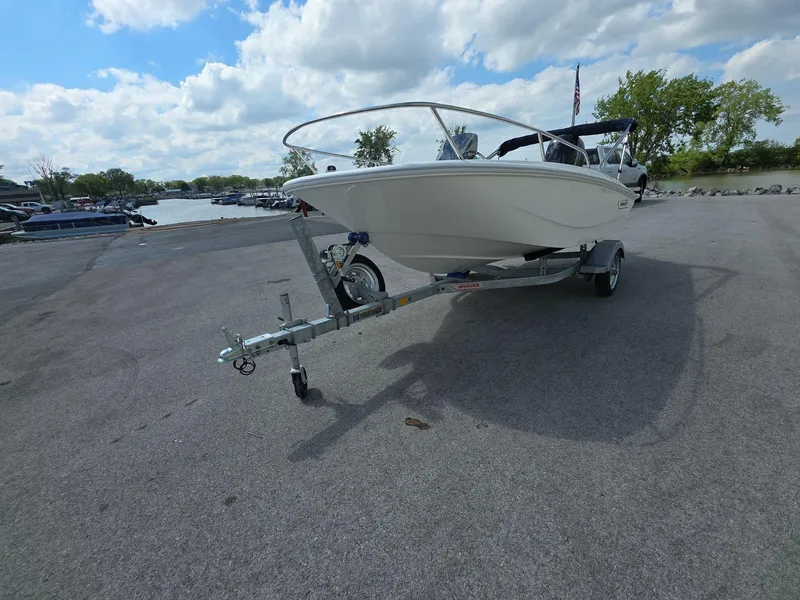 Slide: The Image of 2025 Boston Whaler 130 Super Sport boat on trailer, parked near a lake under a cloudy sky. - 4