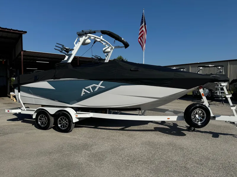 Slide: The Image of 2025 ATX Surf Boats 22 Type-S on trailer, parked outdoors with American flag in background. - 11