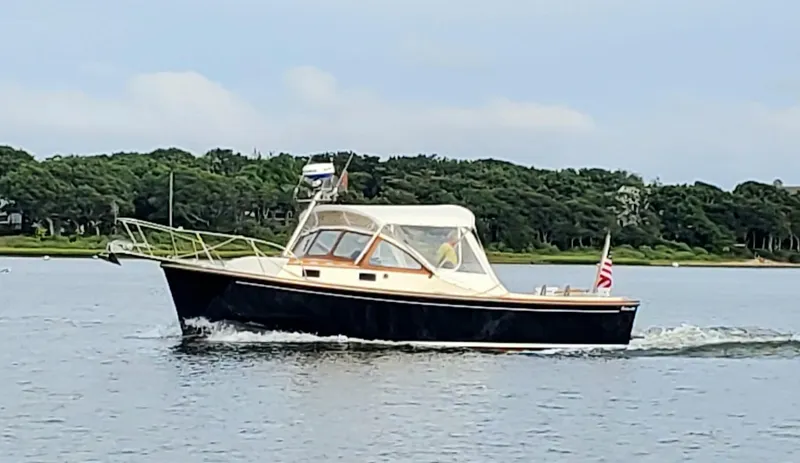 Slide: The Image of 1983 Fortier 26 boat cruising on a calm lake with lush green shoreline. - 47