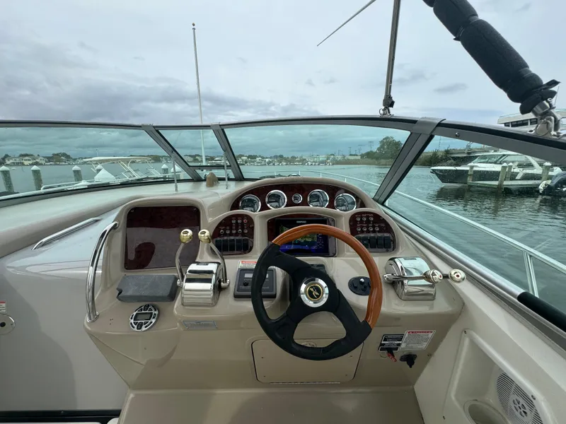 Slide: The Image of 2003 Sea Ray 320 Sundancer helm with steering wheel and controls, docked by the water. - 24