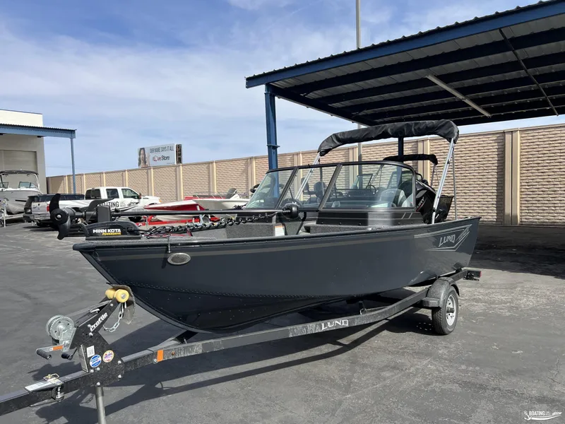 Slide: The Image of 2025 Lund 1650 Angler Sport boat on trailer, parked outdoors under a canopy. - 1
