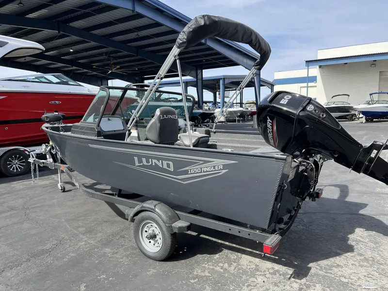 Slide: The Image of 2025 Lund 1650 Angler Sport boat with Mercury engine on trailer, parked outdoors. - 2