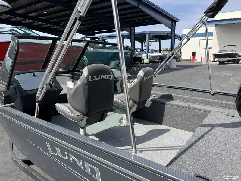 Slide: The Image of 2025 Lund 1650 Angler Sport boat interior with seats and windshield, parked outdoors. - 3