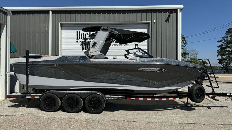 Slide: The Image of 2025 Nautique Paragon 25 boat on trailer outside a warehouse. - 0