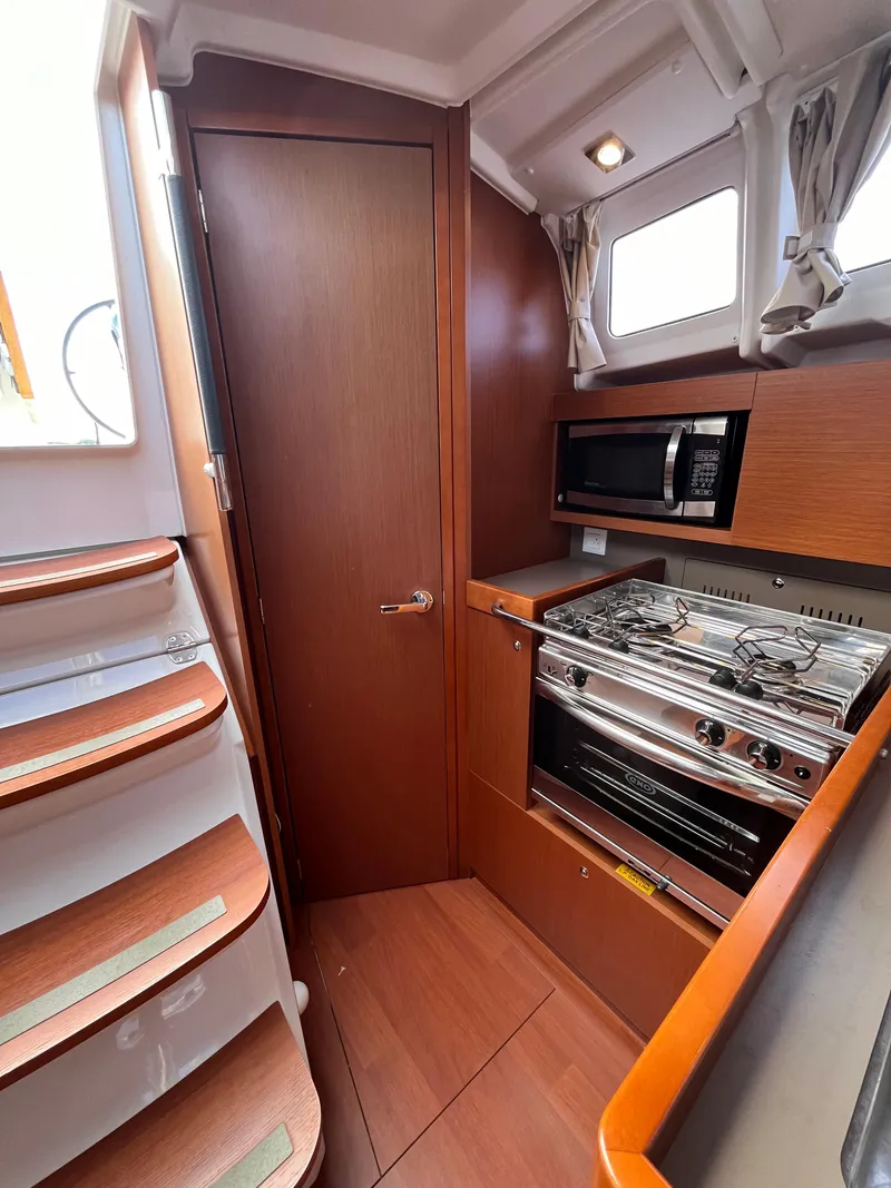 Slide: The Image of 2018 Beneteau Oceanis 35.1 yacht interior kitchen with stove, microwave, and wooden cabinetry. - 31