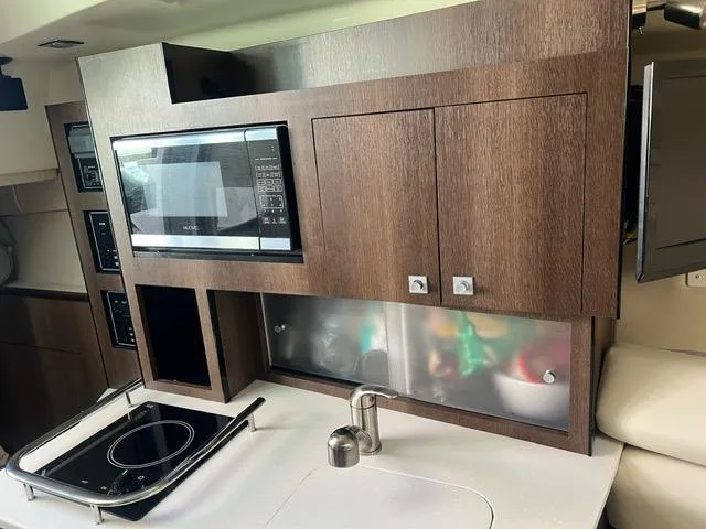 Slide: The Image of 2017 Monterey 295 Sport Yacht kitchen with microwave, stove, and wooden cabinetry. - 9