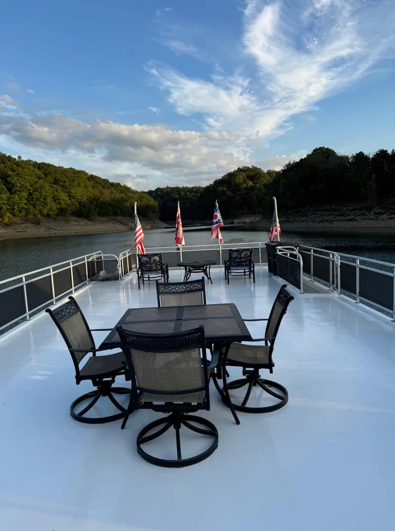 Slide: The Image of 2004 Sumerset 20x100 houseboat deck with outdoor seating, flags, and scenic lake view. - 12