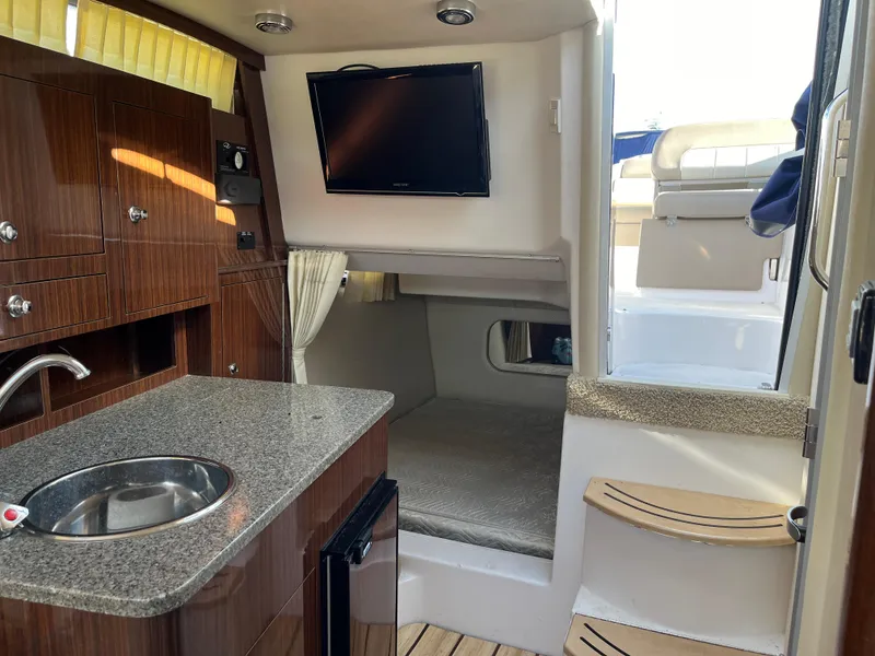 Slide: The Image of 2013 Regal 30 Express boat interior with kitchenette, TV, and cozy seating area. - 19
