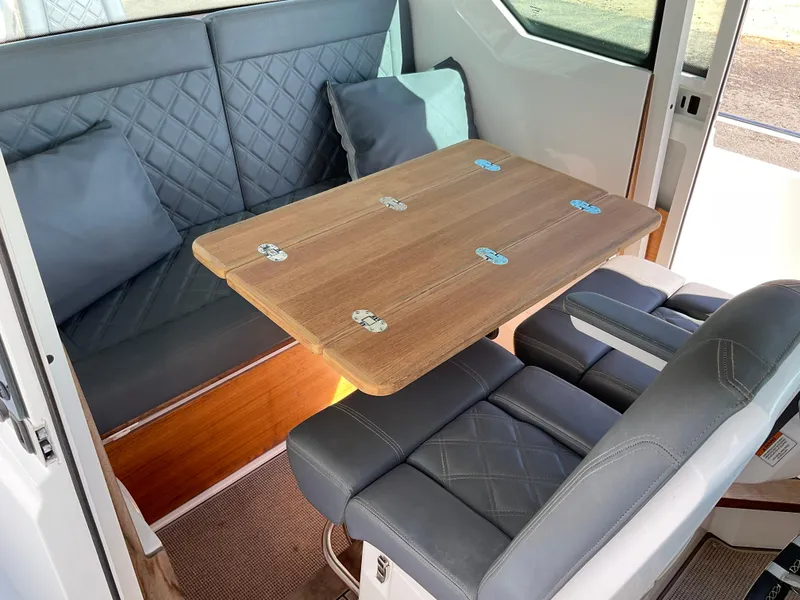 Slide: The Image of 2020 Axopar 28 interior with quilted seating and wooden table. - 18