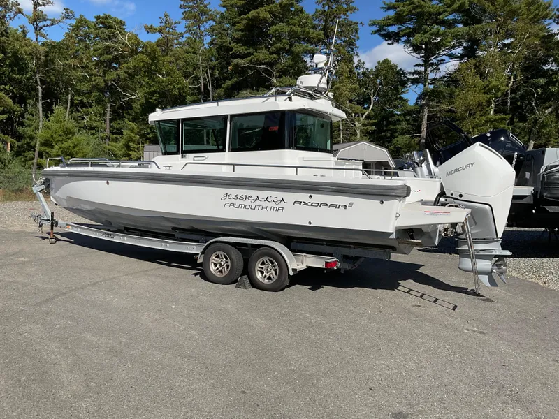 Slide: The Image of 2020 Axopar 28 boat on trailer, parked outdoors with trees in the background. - 3