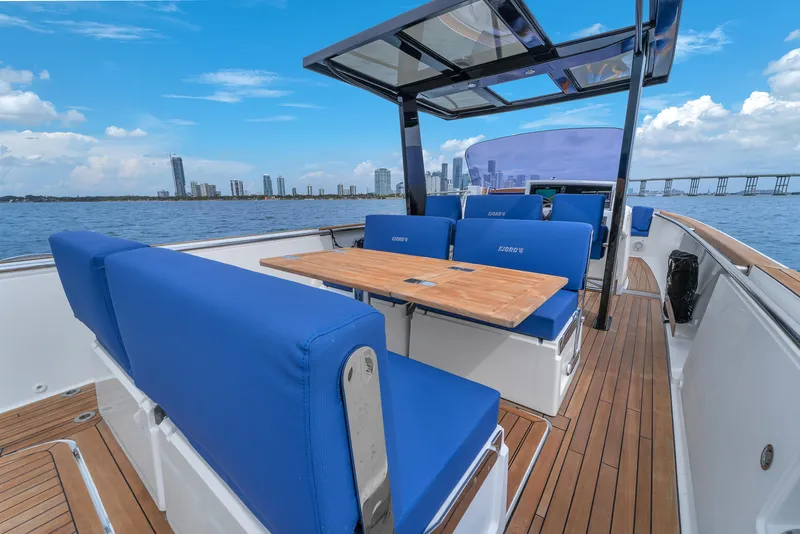Slide: The Image of 2019 Fjord 38 Xpress boat with blue seating, wooden deck, and city skyline in the background. - 45