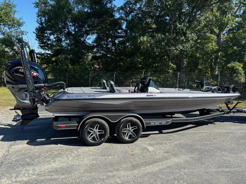 Slide: The Image of 2025 Skeeter ZXR 21 boat on trailer, parked outdoors, with trees in the background. - 2