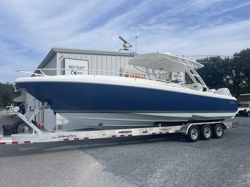 Slide: The Image of 2013 Intrepid 327 Cuddy boat on trailer, blue and white, parked outdoors. - 16