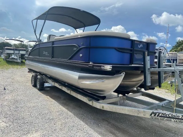 Slide: The Image of 2023 Barletta Cabrio 24 UC pontoon boat on trailer, blue and black design, parked outdoors. - 3