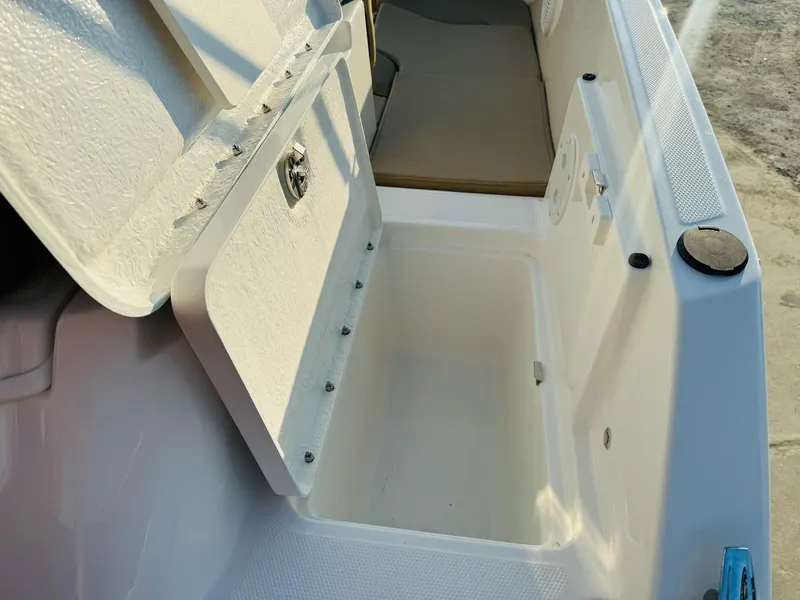 Slide: The Image of 2025 Bayliner VR6 Bowrider OB storage compartment, open lid, white interior, outdoor setting. - 11