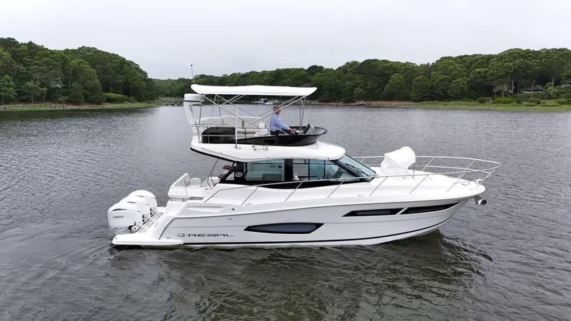 Slide: The Image of 2025 Regal 38 FXO yacht cruising on a serene lake with lush green surroundings. - 1