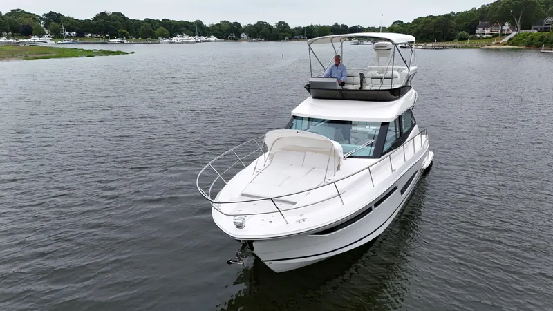 Slide: The Image of 2025 Regal 38 FXO yacht cruising on a serene lake with lush greenery. - 3