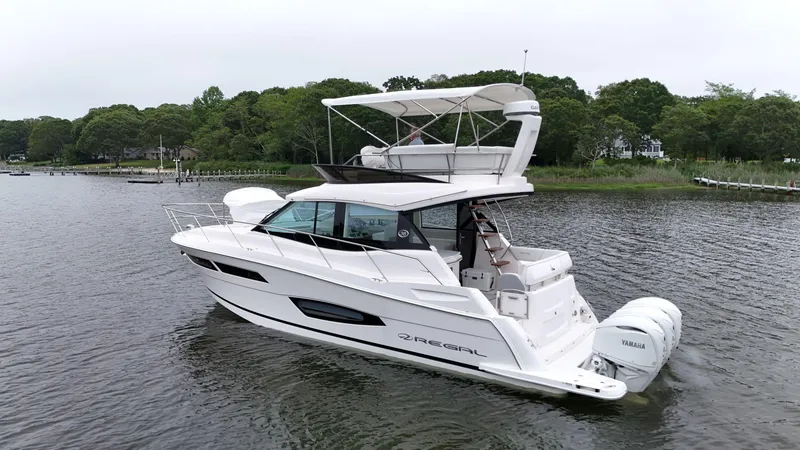 Slide: The Image of 2025 Regal 38 FXO yacht on a serene lake with lush green shoreline. - 6