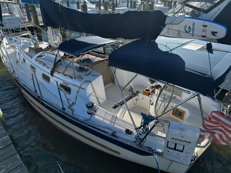 Slide: The Image of 2006 Pacific Seacraft 31 sailboat docked, featuring blue canvas covers and a spacious cockpit. - 2