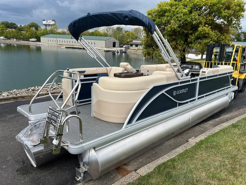 Slide: The Image of 2025 Godfrey SWEETWATER 2286 SB pontoon boat docked by a serene lakeside. - 5