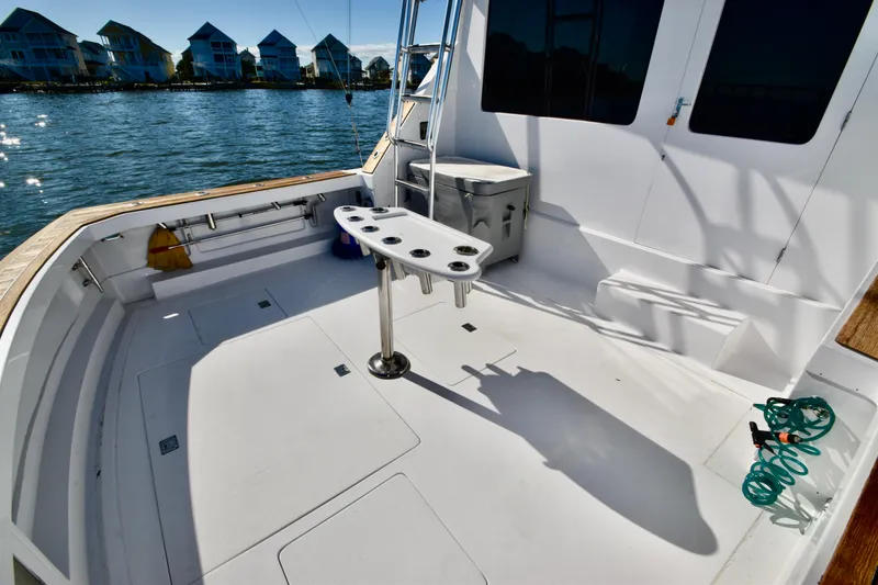 Slide: The Image of 1982 Bertram 46 Convertible boat deck with fishing rod holders, docked by waterfront homes. - 25