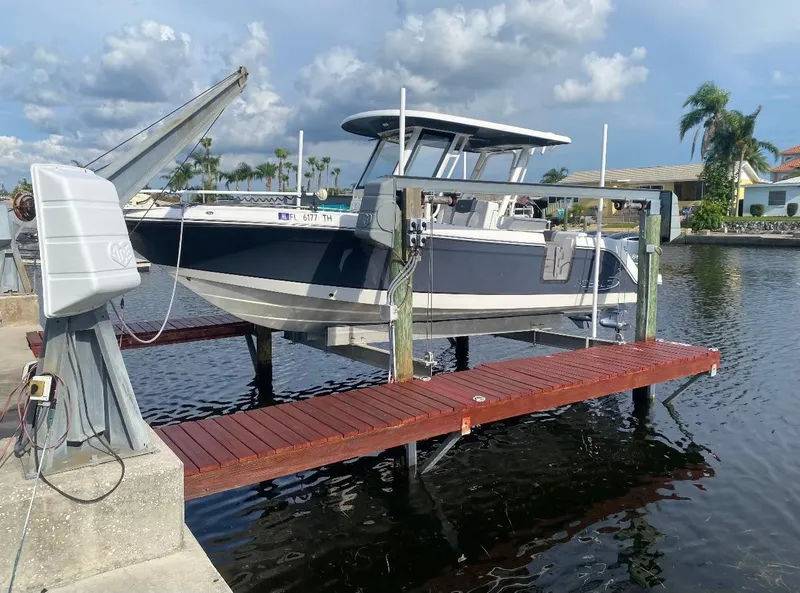 The Image of 2021 Robalo R272 Center Console boat docked on a lift by the water. - 1
