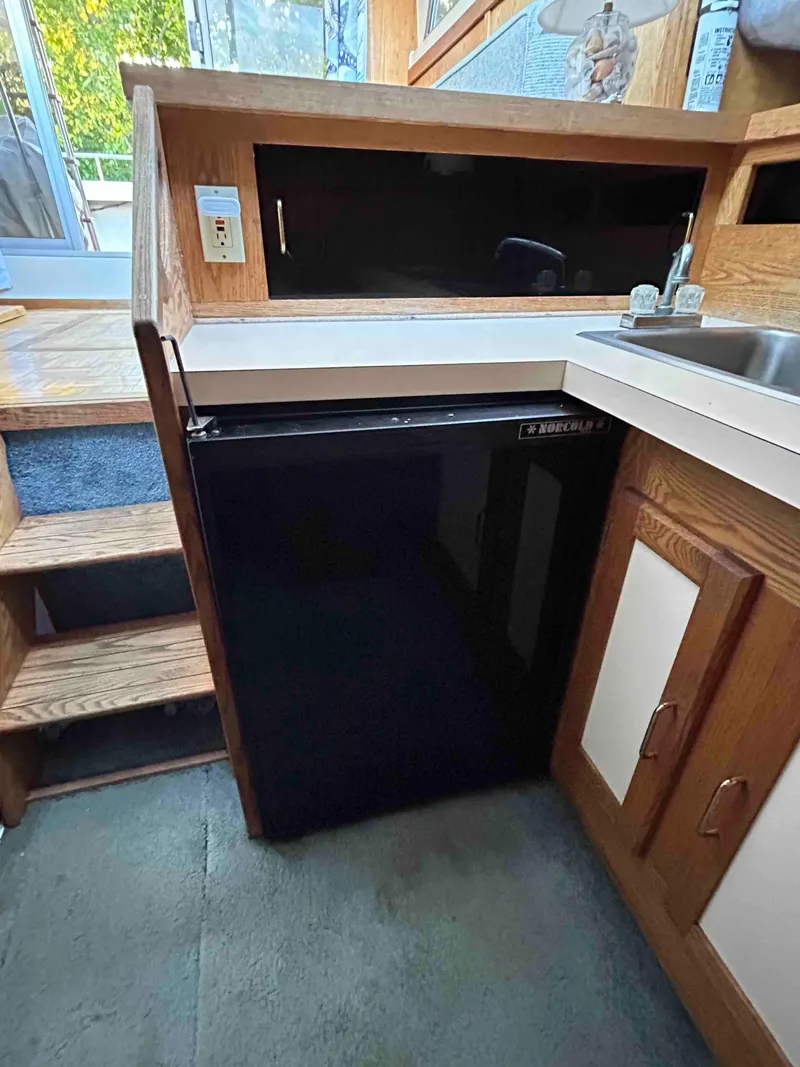 Slide: The Image of 1986 Silverton 31 Convertible interior with kitchenette, featuring a compact fridge and wooden cabinetry. - 13
