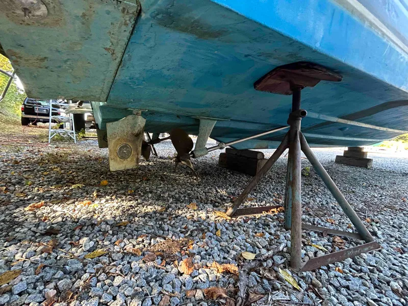 Slide: The Image of 1986 Silverton 31 Convertible boat on stands, showing hull and propeller, resting on gravel. - 24