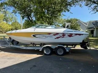 The Image of 2001 Baja 232 speedboat on trailer, white with red and yellow accents, parked outdoors. - 0