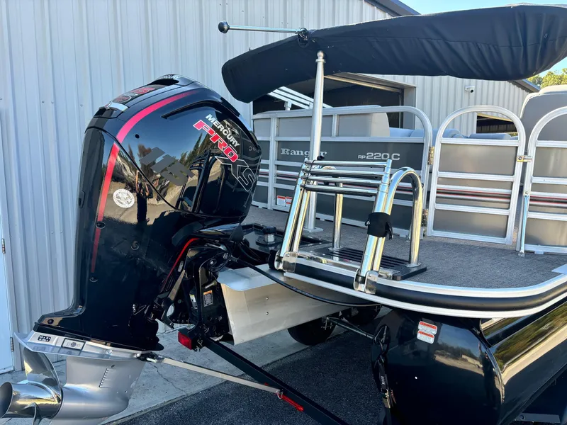 Slide: The Image of 2023 Ranger Reata 220C pontoon boat with Honda outboard motor, docked near a metal building. - 11