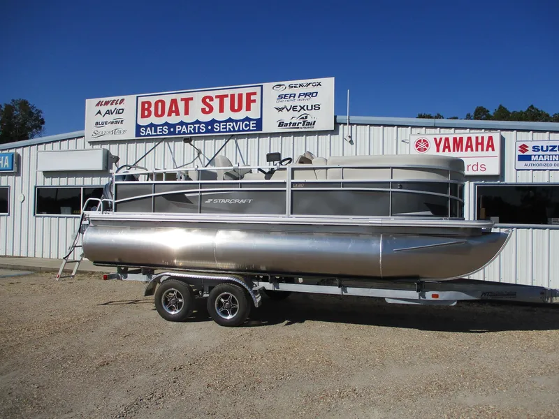 The Image of 2025 Starcraft LX 20 CB pontoon boat on trailer outside dealership. - 0