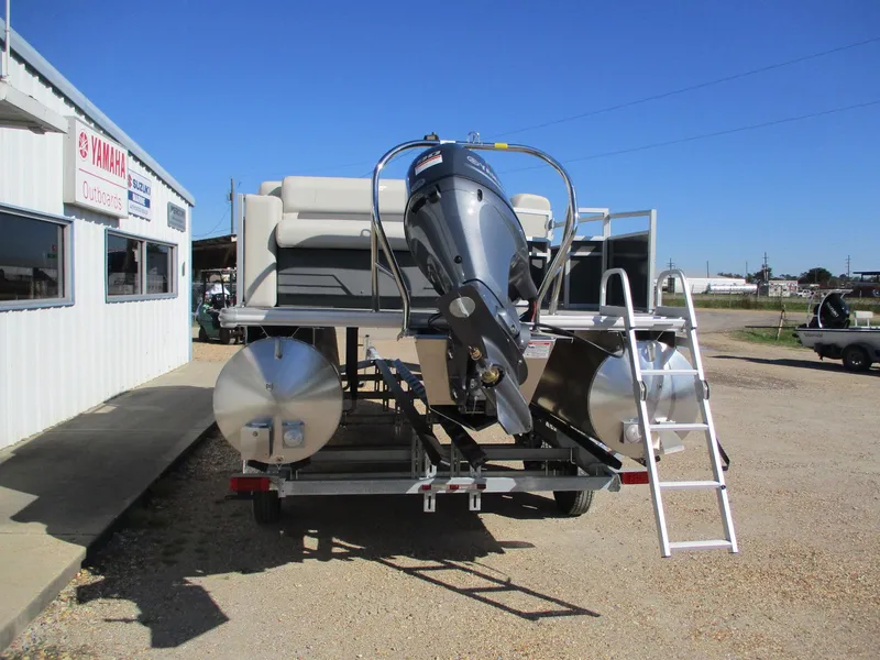 Slide: The Image of 2025 Starcraft LX 20 CB pontoon boat with outboard motor and ladder, parked outside dealership. - 5