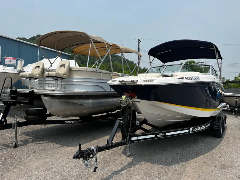 Slide: The Image of 2021 Cobalt 23SC boat on trailer beside pontoon boat in outdoor lot. - 2