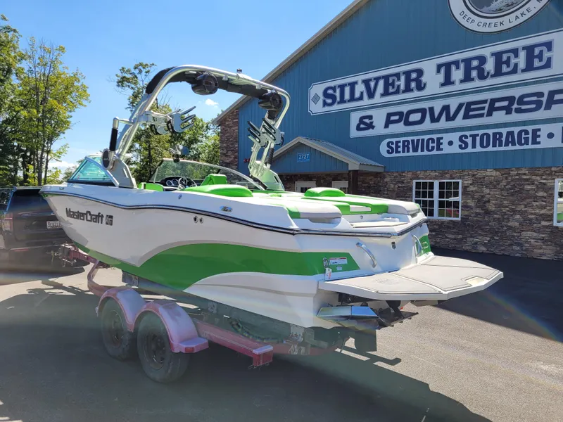 Slide: The Image of 2019 MasterCraft XT23 boat with green accents on a trailer outside Silver Tree & Powersports. - 2