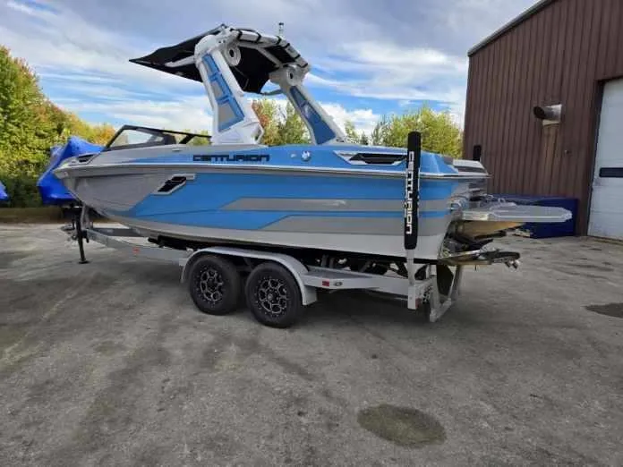 Slide: The Image of 2023 Centurion Ri230 boat on trailer, blue and white design, parked outdoors. - 5