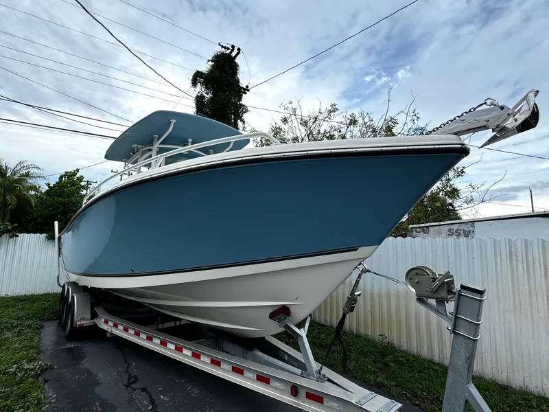 Slide: The Image of 2020 Mako 284 CC boat on trailer, blue hull, parked outdoors. - 2
