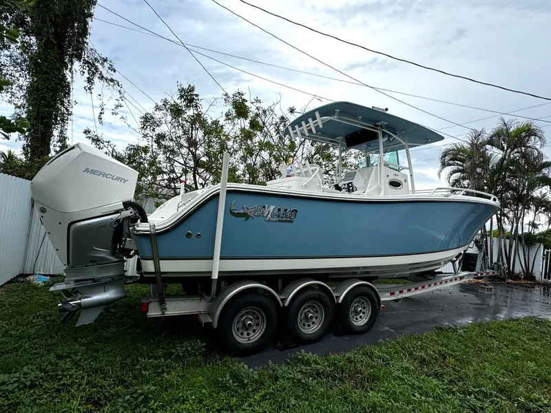 Slide: The Image of 2020 Mako 284 CC boat on trailer, blue hull, triple-axle, Mercury engine, parked outdoors. - 4