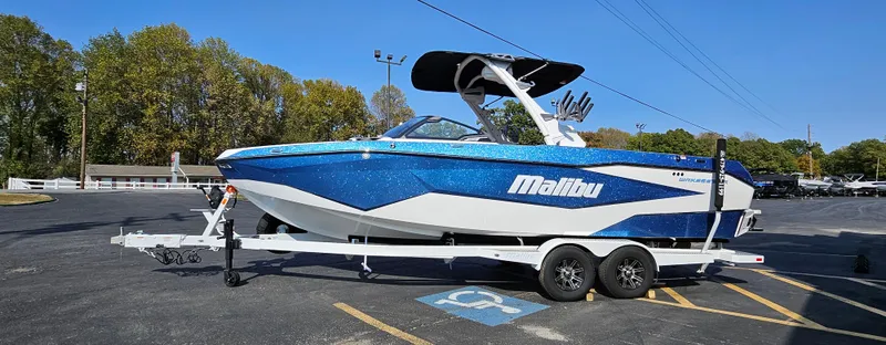 Slide: The Image of 2025 Malibu 25LSV boat in blue and white on a trailer in a parking lot. - 1